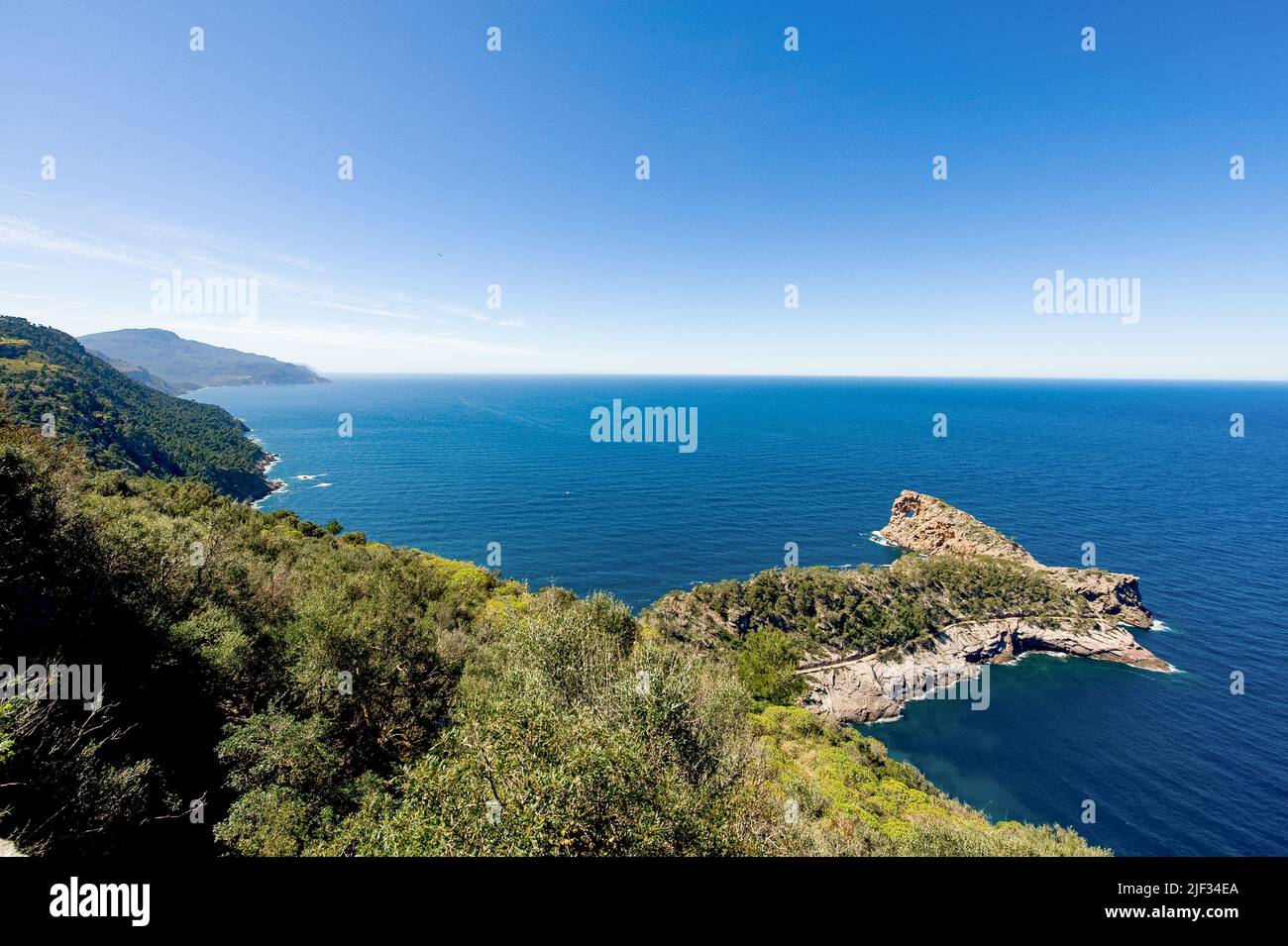 Weite Sicht auf das Meer mit klarem blauen Himmel und ruhigem Meer. Blick von einem hohen Aussichtspunkt. Sichtbare, bewaldete Felsen. Stockfoto