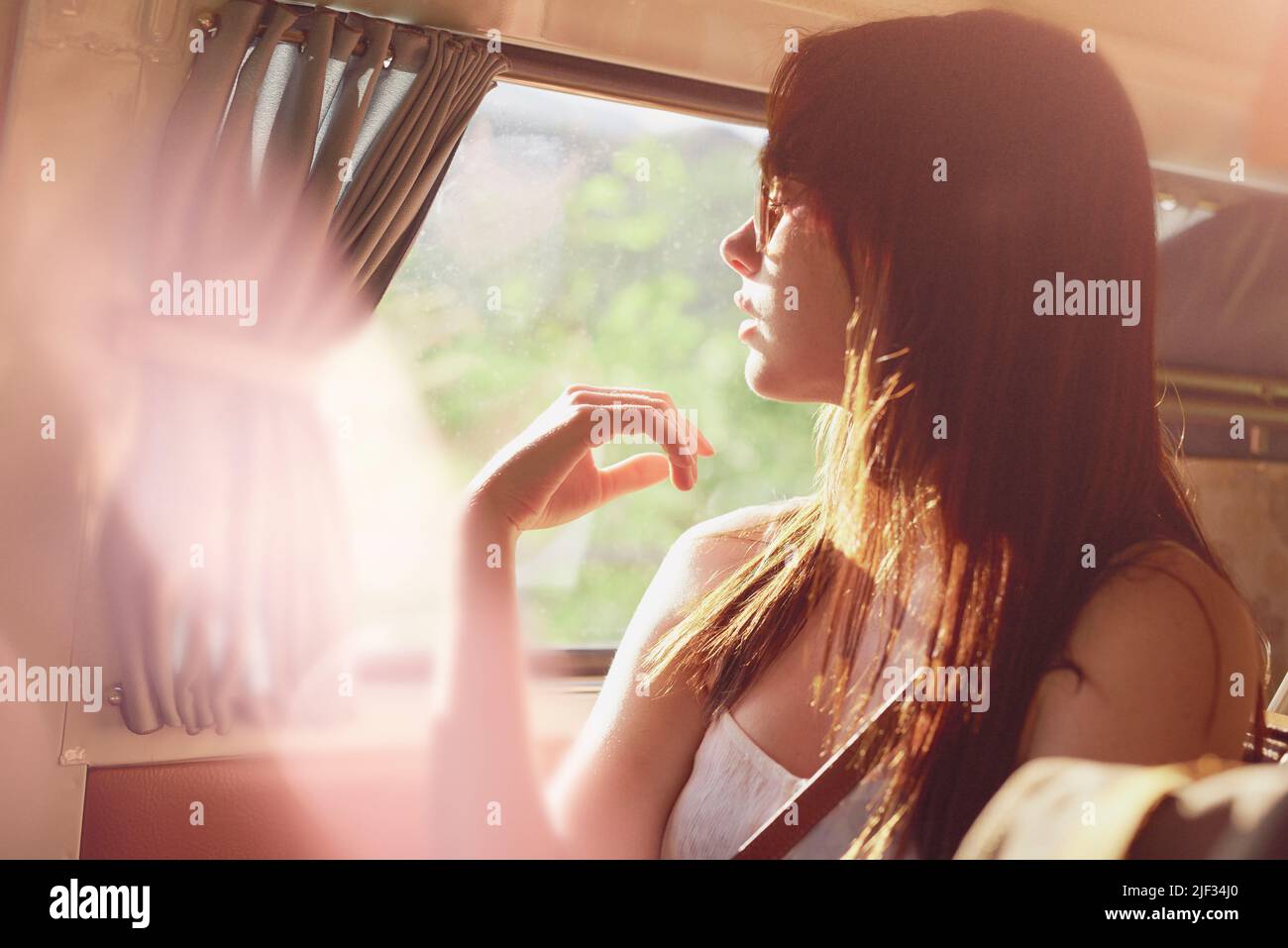 Eine unbeschwerte junge Frau in ihrem Wohnmobil genießt die Wärme der Sonne. Junge Frau auf einem Roadtrip, die in ihrem Van sitzt und die Sonne genießt. Inhalte jung Stockfoto