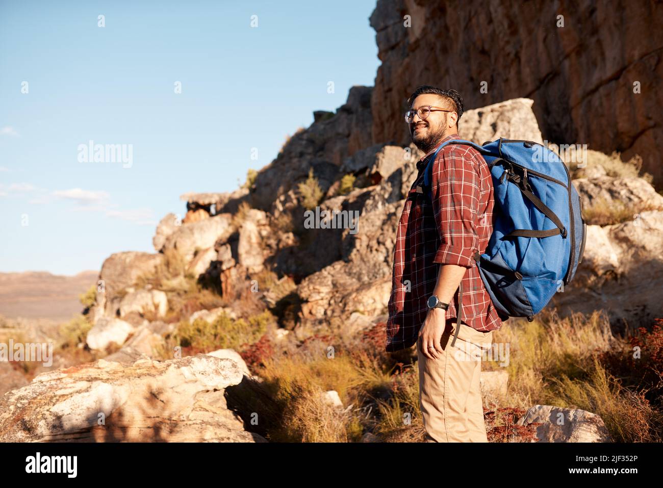 Ein junger erwachsener Mann starrt auf die Aussicht von den felsigen Bergen auf einem Wanderausflug Stockfoto