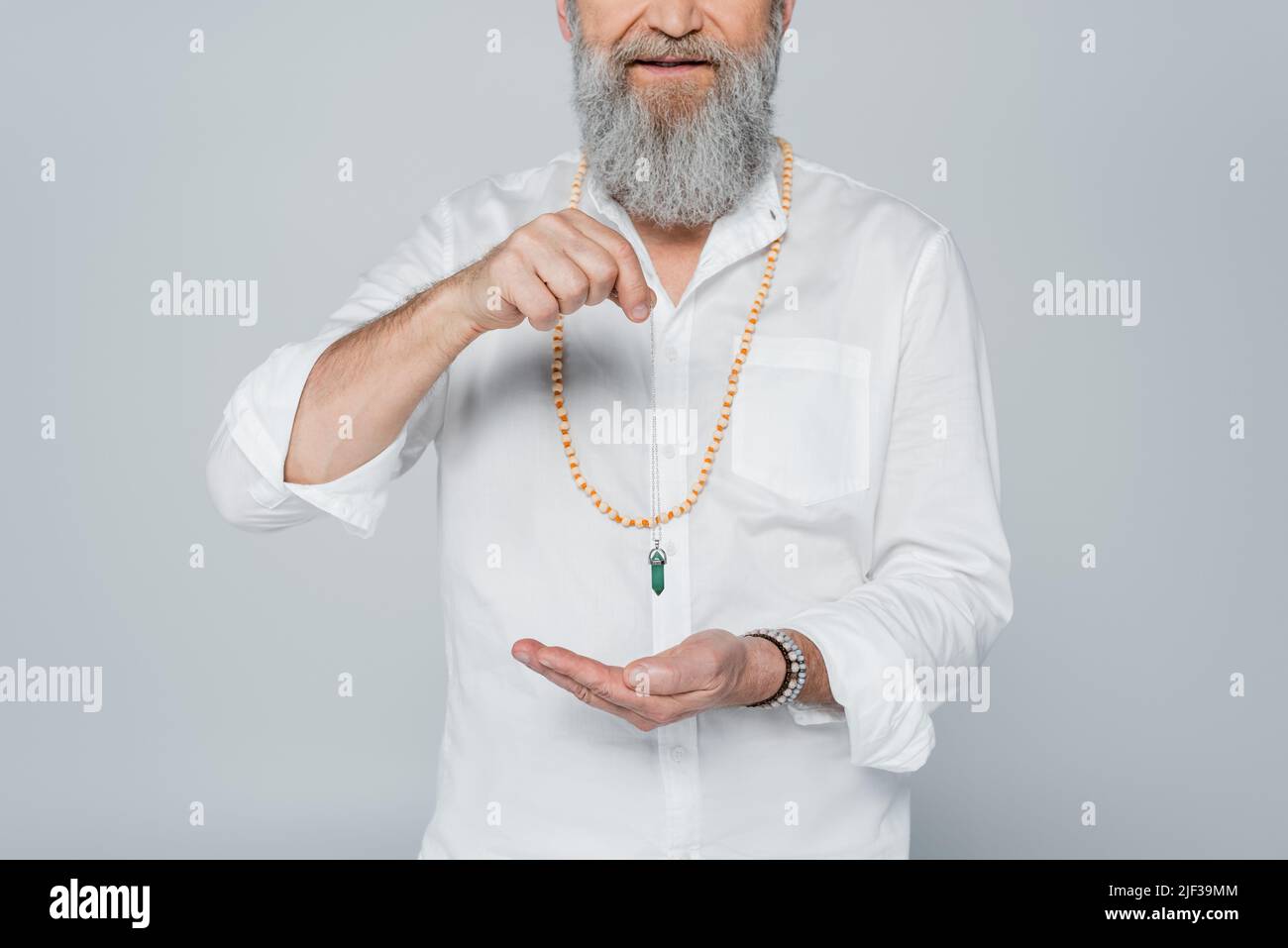 Partielle Ansicht eines bärtigen spirituellen Gurus, der das Pendel in der Hand hält, isoliert auf Grau Stockfoto