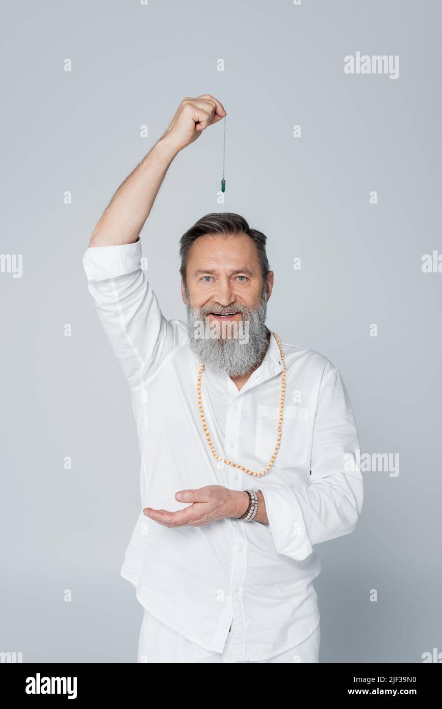 Positiver Meisterguru mit Pendel, das die Kamera isoliert auf Grau anschaut Stockfoto