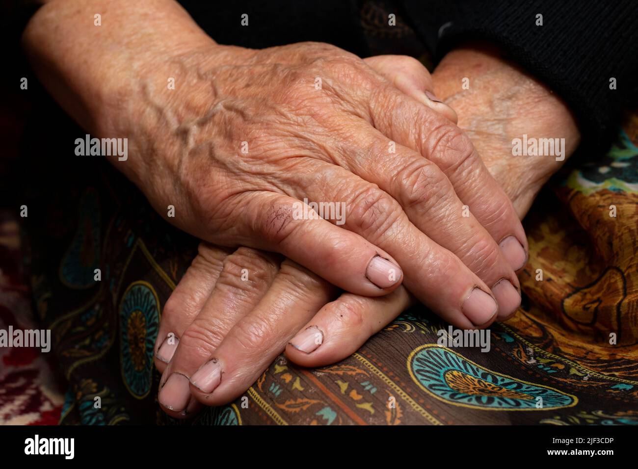 Großmutter sitzt mit den Händen auf ihrem Schoß, auf dunklem Hintergrund Stockfoto