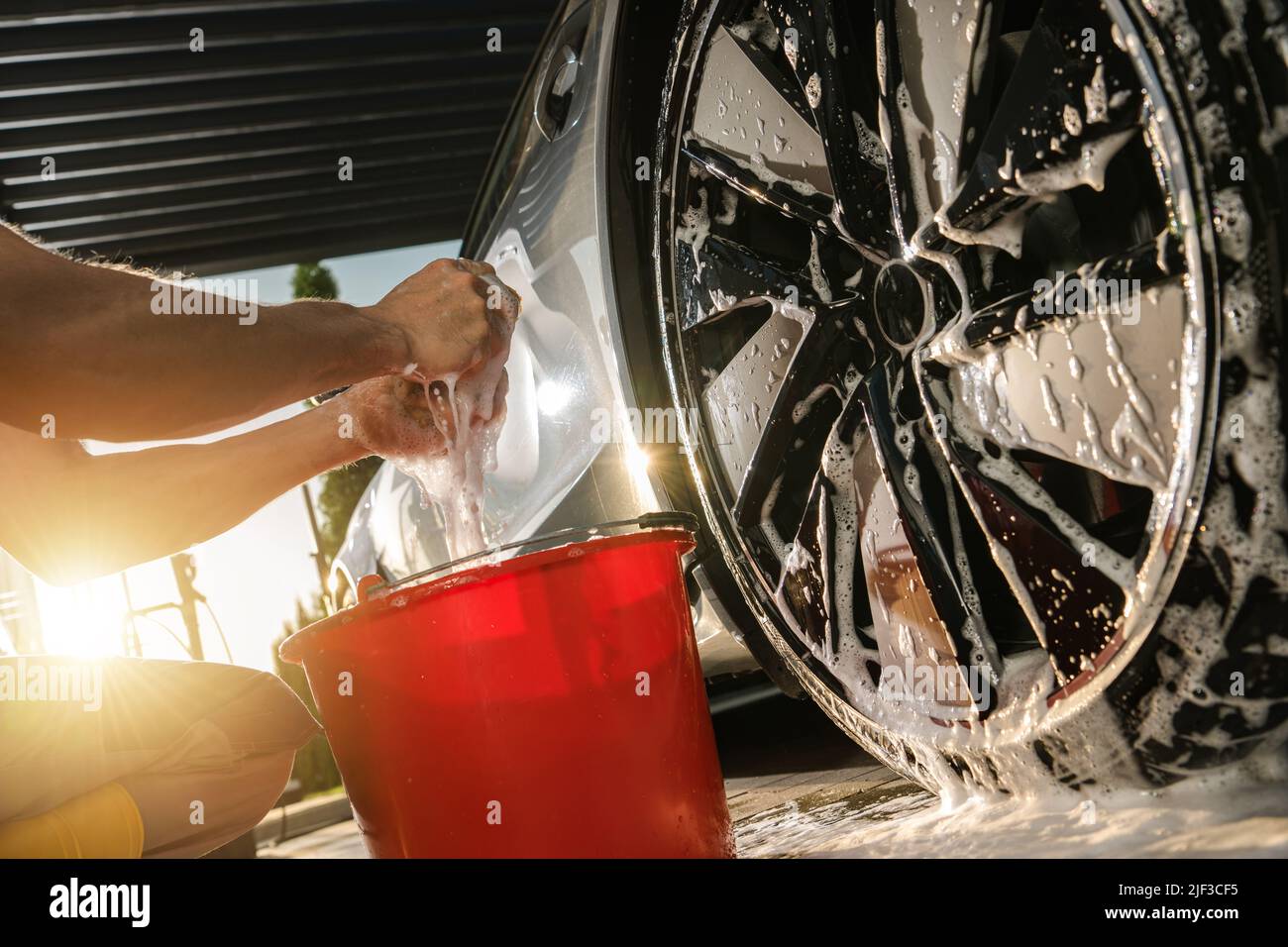 Kaukasische Männer Reinigung moderner Auto-Legierung Räder auf seiner Auffahrt mit Spezialwaschmittel und weichen Sponge. Thema Fahrzeugwartung, Stockfoto