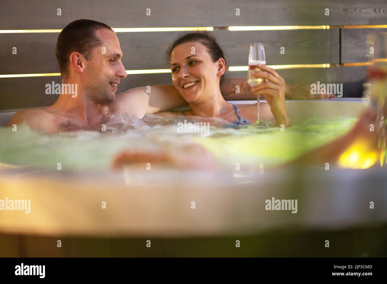 Kaukasisches Paar in ihren 40s, die romantische Zeit in ihrem Garten Whirlpool Spa während des warmen Sommerabends haben. Freizeit- und Wellness-Thema. Stockfoto