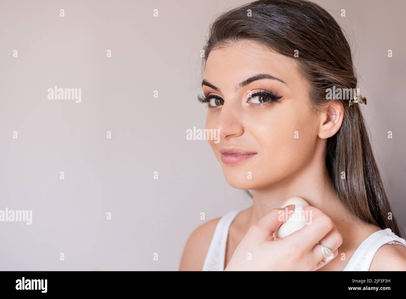 Schöne kaukasische Modell Nahaufnahme schauen gerade und lächeln während Make-up Session. Die Make-up-Künstlerin setzt das Fundament auf den Hals. Der Stockfoto