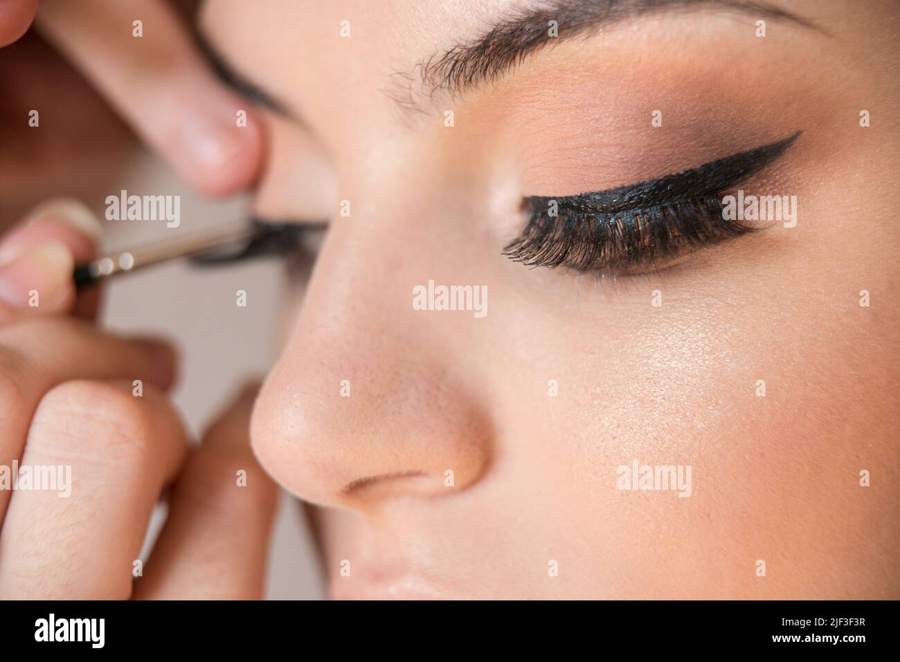 Makrodetails von falschen Wimpern des kaukasischen Modells während der Make-up-Sitzung. Der Make-up-Künstler wendet mit dem Pinsel einen schwarzen Eyeliner an. Das Modell verfügt über Stockfoto