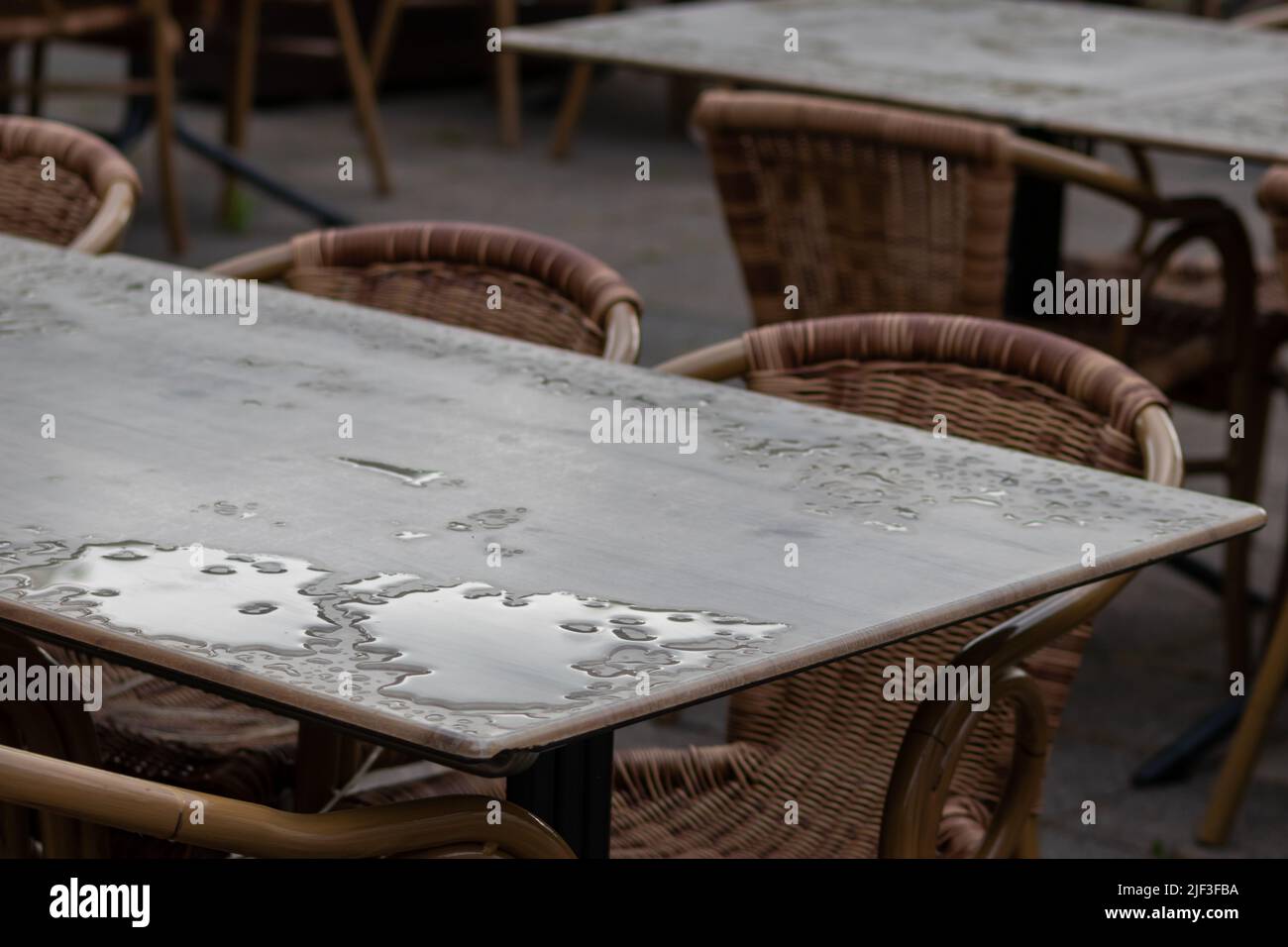 Leerer Tisch und leere Stühle im Sommer Restaurant oder Biergarten im Sommer an regnerischen Tagen mit Regentropfen und keine Gäste, kein Einkommen auf Bürgersteig Sitzgelegenheiten Stockfoto