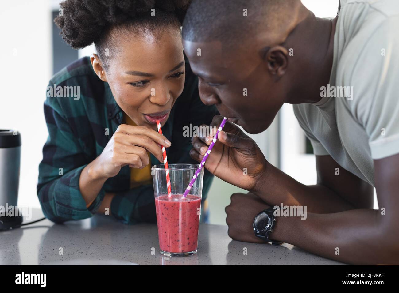 Glückliches afroamerikanisches Paar mittlerer Erwachsenen, das sich ansieht, während es in der Küche Smoothie trinkt Stockfoto
