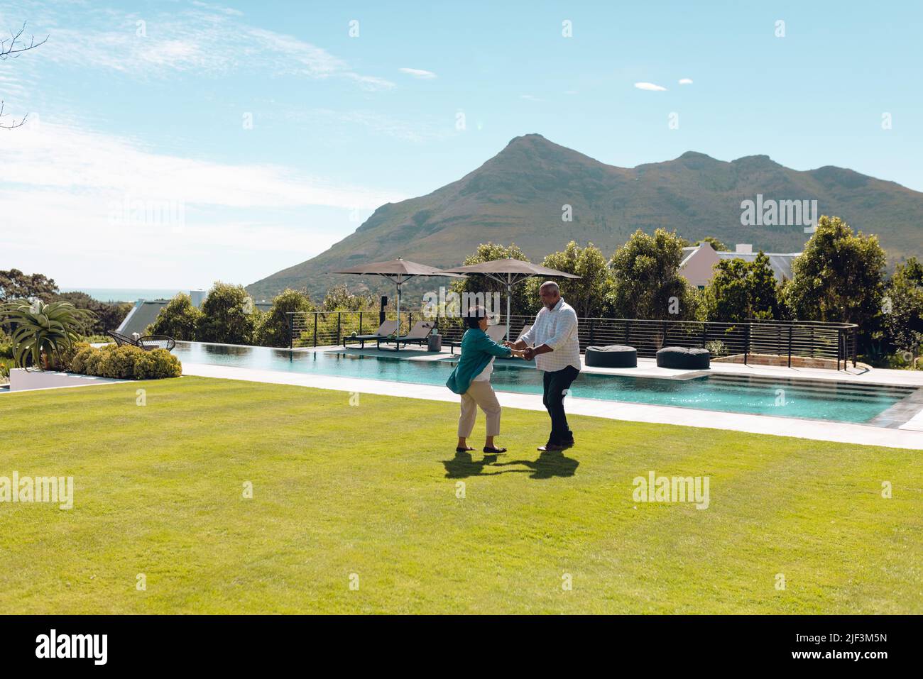 Ältere Freunde der Biracial tanzen im Pool im Garten gegen Berg und Himmel Stockfoto