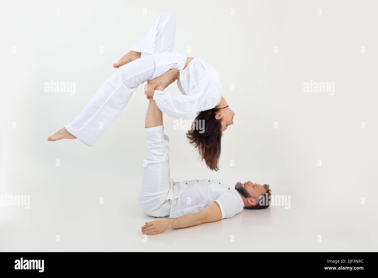 Aktive und sportliche Familie von Mann und Frau, die Yoga, Pilates und Fitness praktiziert, wobei der Mann die Frau an den Beinen zurück in der Luft hält Stockfoto