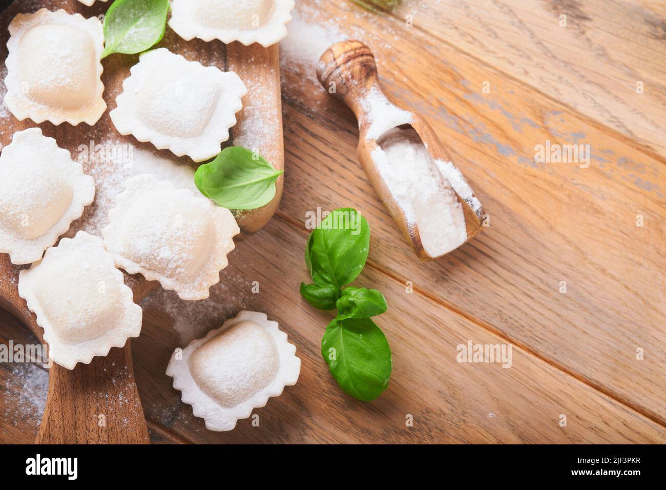 Ravioli, italienische Küche. Leckere hausgemachte Pasta-Ravioli mit Mehl, Tomaten, Eiern und grünem Basilikum auf Holzboden. Prozess der Herstellung italienischer Ravioli Stockfoto