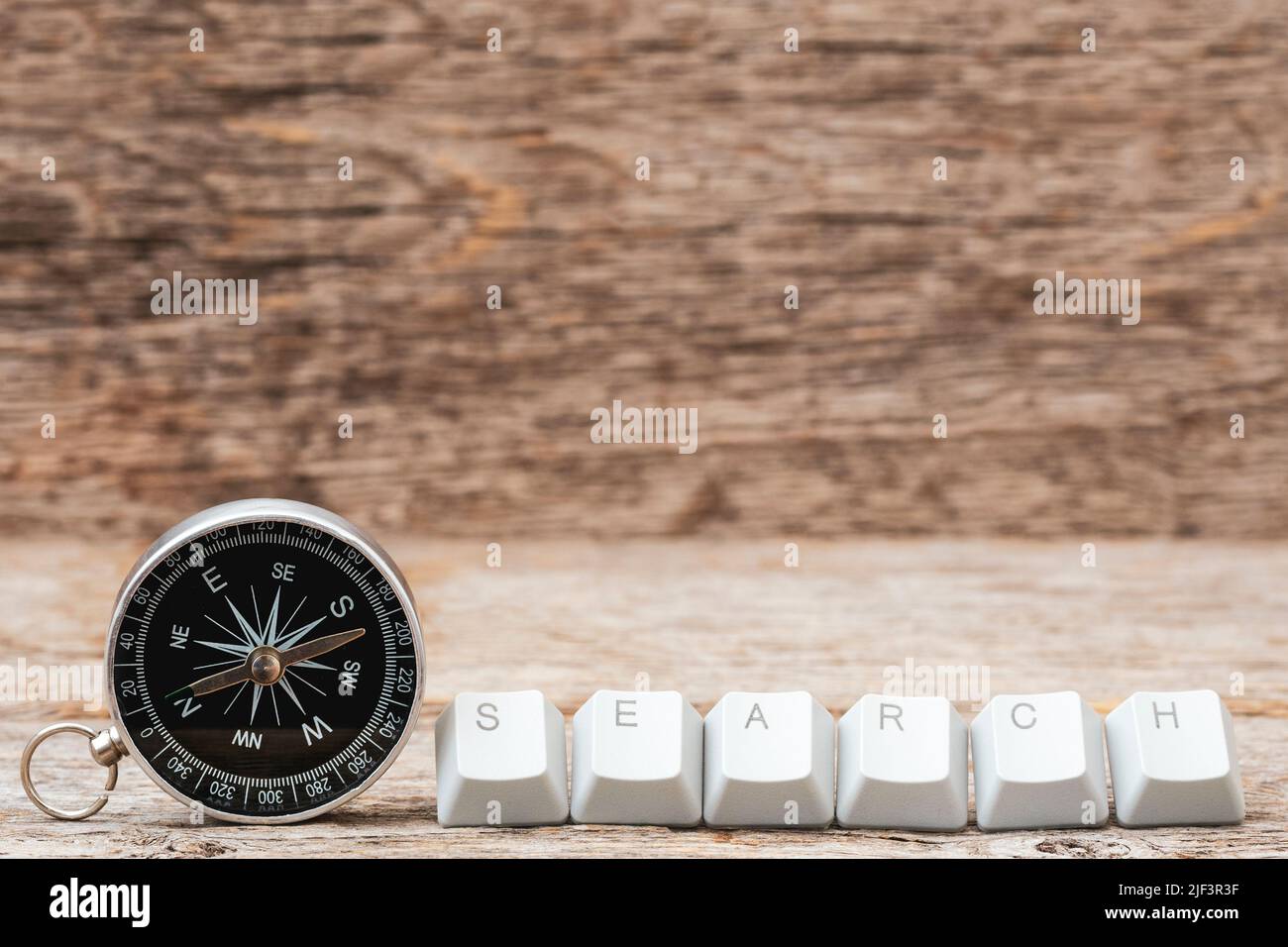 Kompass- und Computertastaturtasten, angeordnet, um Suchwort auf dem hölzernen Hintergrund zu buchstabieren. Durchsuchen Von Internet Data Information Networking Con Stockfoto