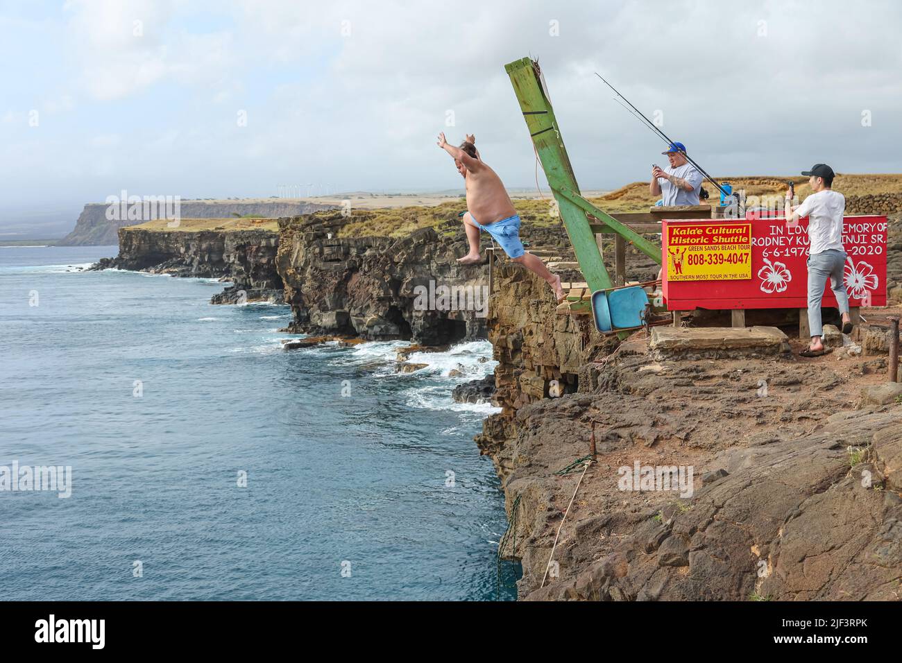 Ein Mann springt von den Klippen des South Point der Big Island ins Meer, während seine Freunde in Hawaii Fotos machen Stockfoto