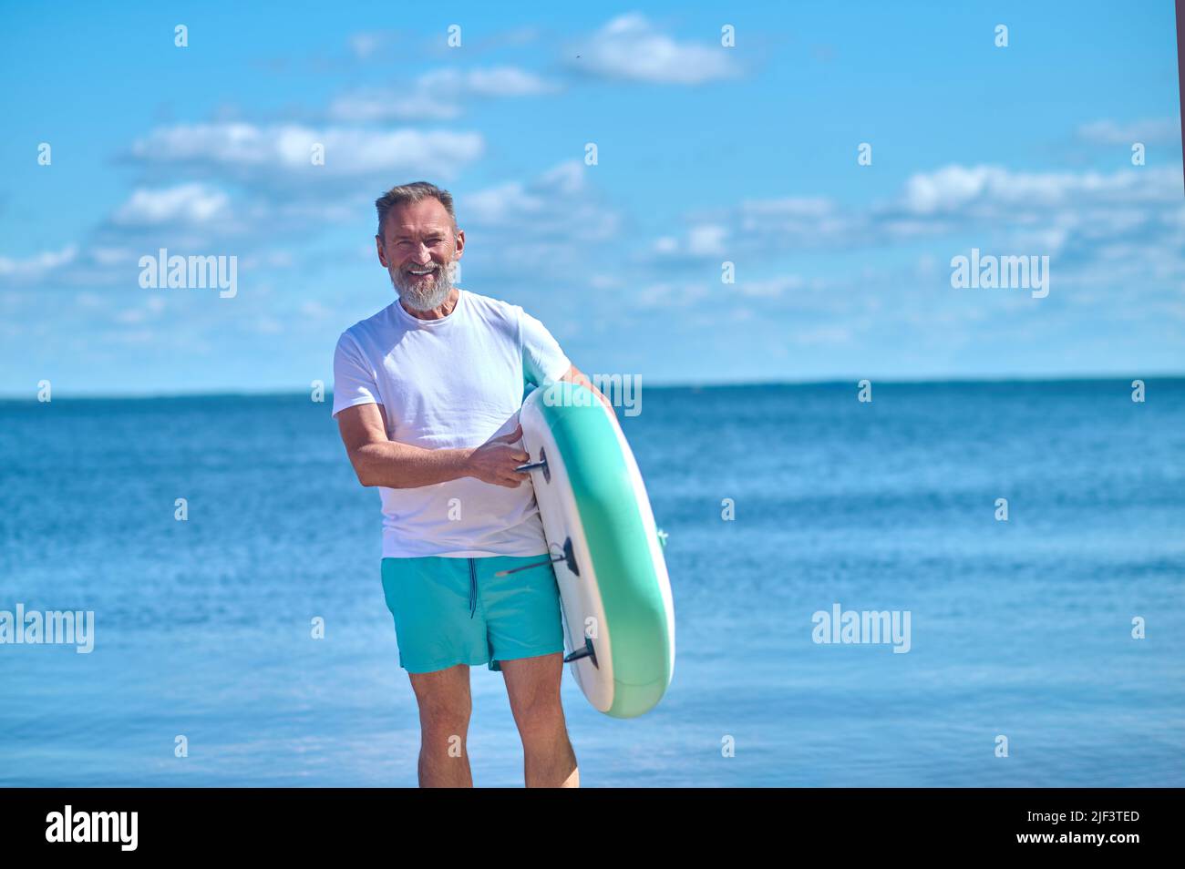 Mann mit aufblasbarem Paddleboard lächelt der Kamera zu Stockfoto