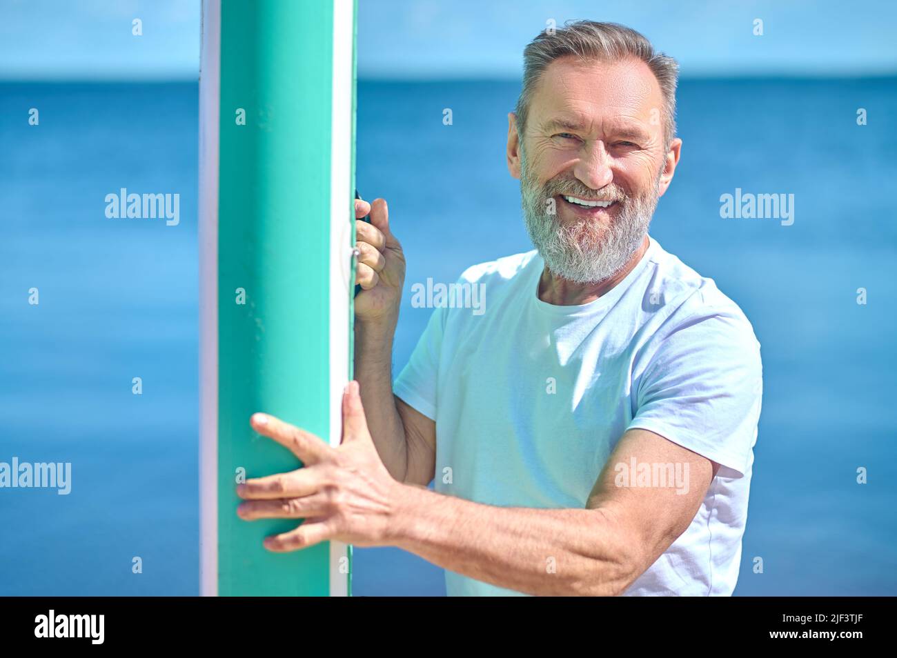 Mann, der das Ruderbrett berührt, lächelt der Kamera zu Stockfoto