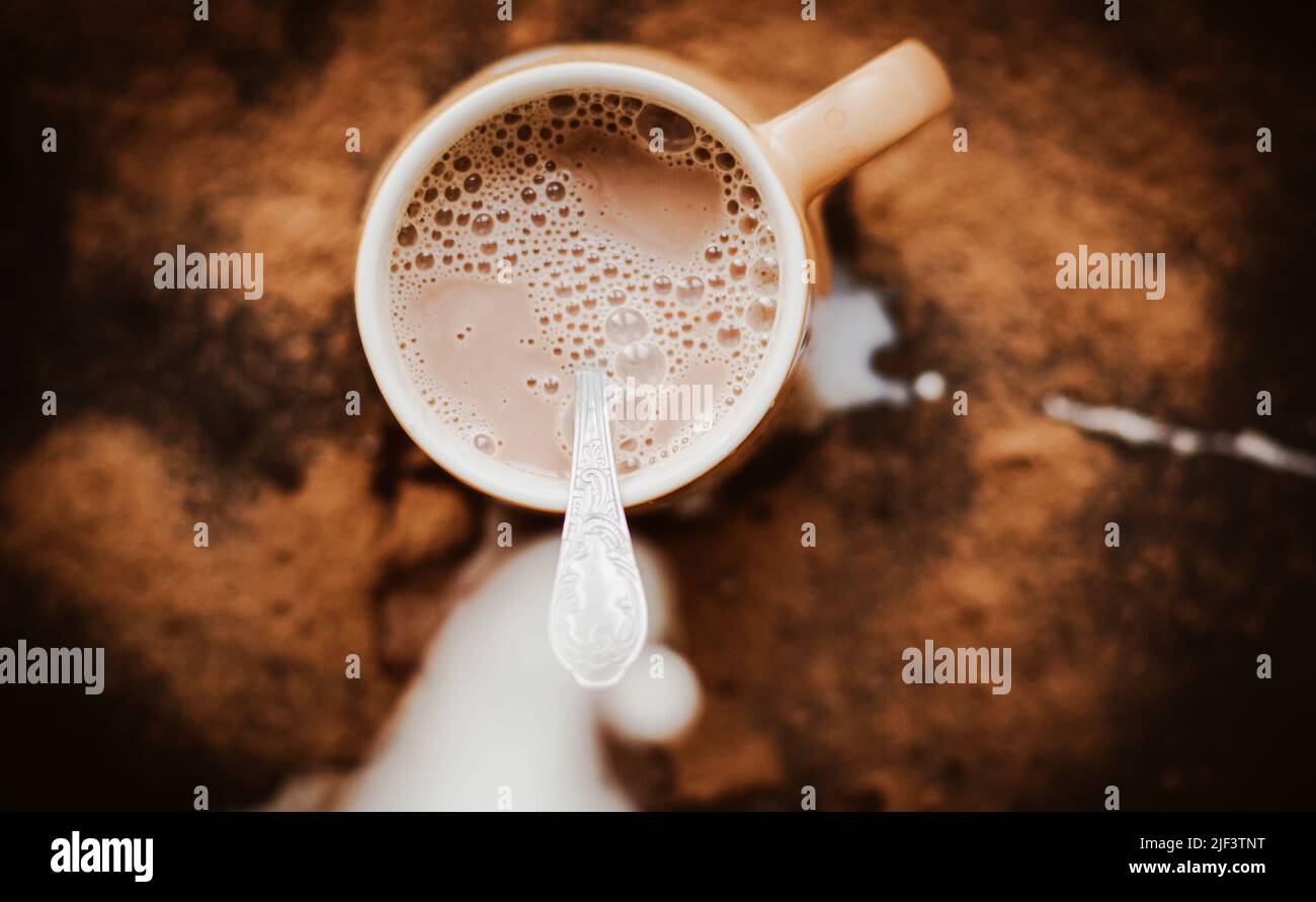 Die Milch wird in einen beigen Becher mit warmem Kakao gegossen, dessen Spritzer auf den Tisch fielen. Chaos in der Küche. Köstlicher Eiskaffee. Stockfoto