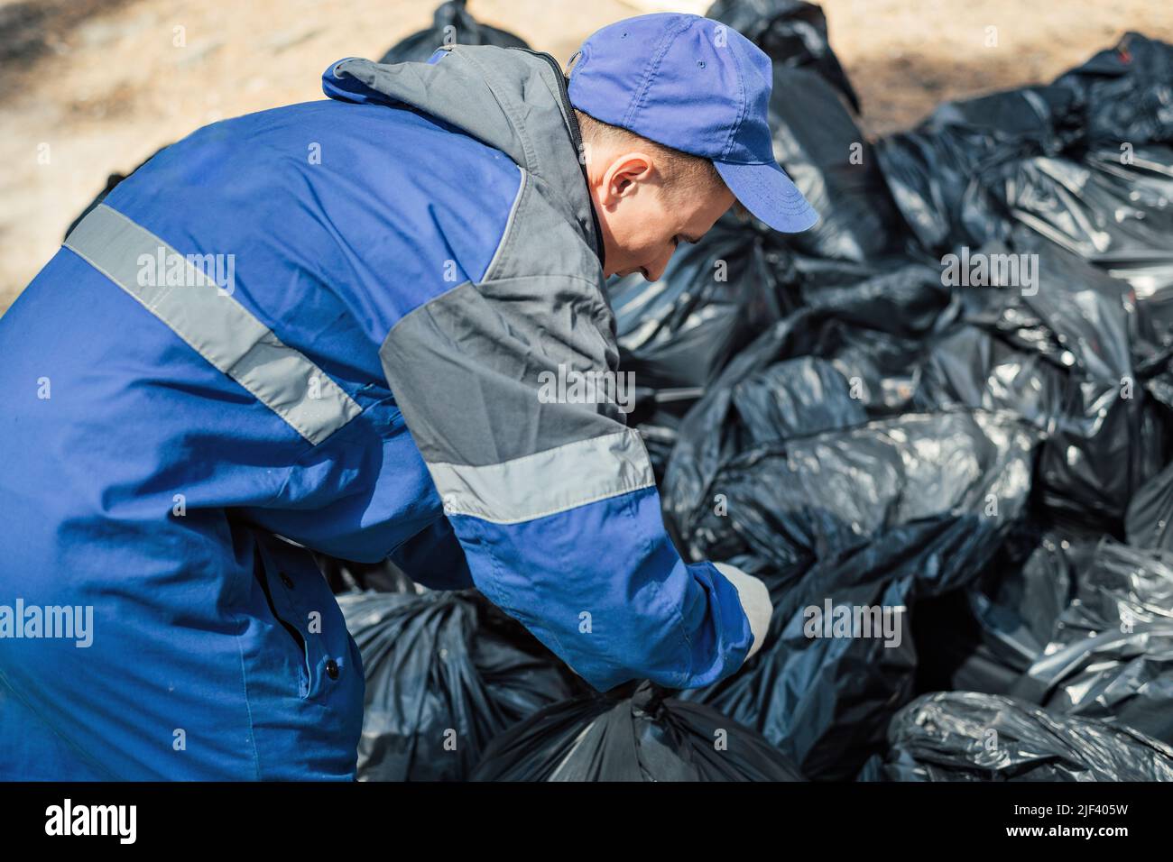 Mann in Overalls bindet Plastiksäcke mit Müll. Ökologische Kampagne der Waldreinigung. Machen Sie die Natur sauberer. Volunteer räumt Müll auf. Stockfoto