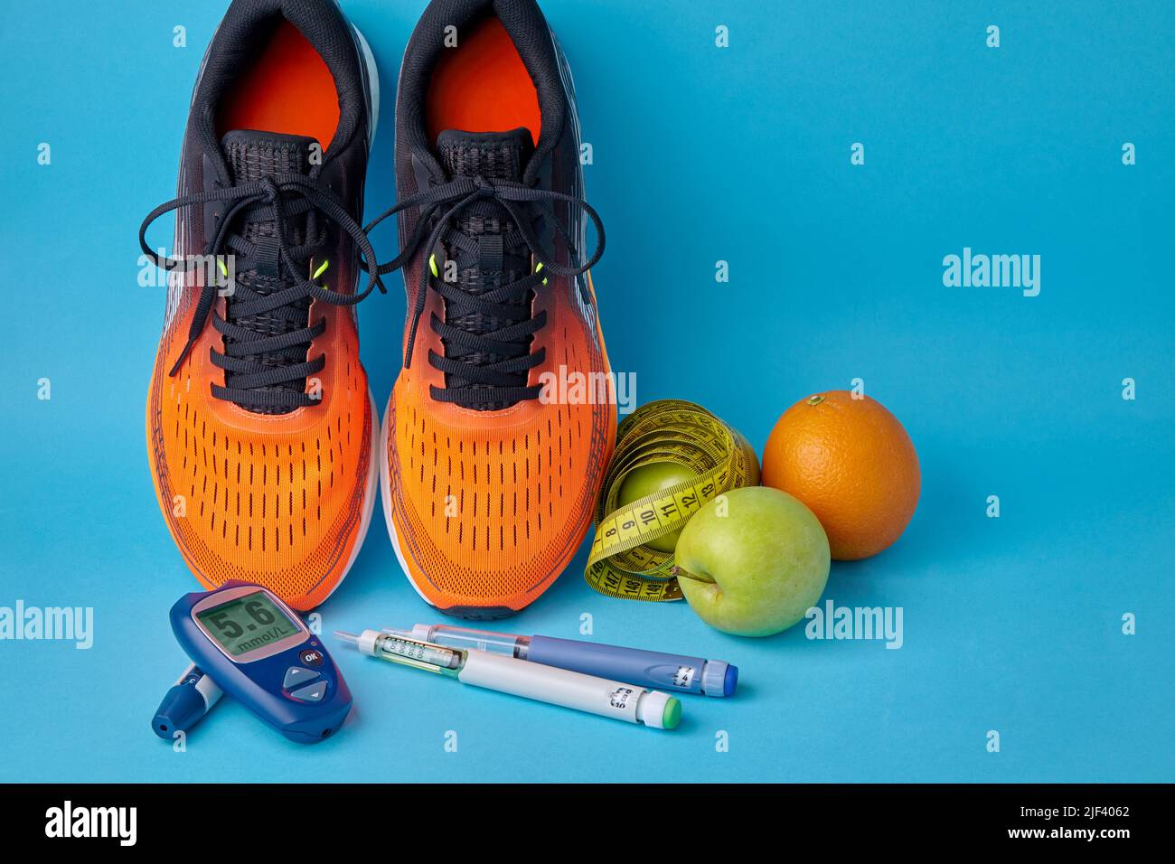 Orangefarbene Sneakers, Früchte, Maßband, Glucometer und Insulin-Spritzenstifte auf blauem Hintergrund Stockfoto