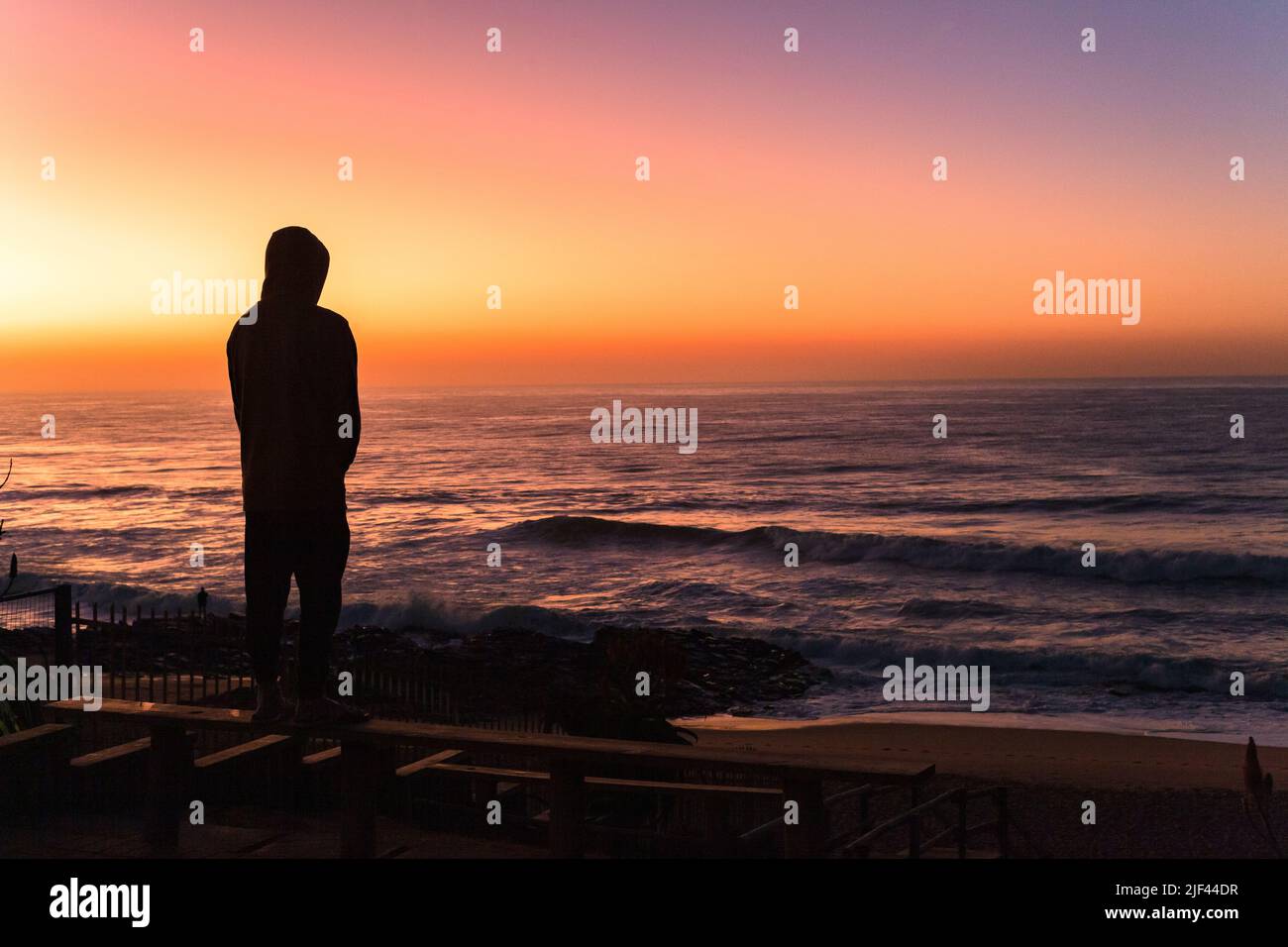 Morgendämmerung mit Blick auf den Strand Ozean mit Mann Figur Silhouetten Blick auf den Horizont mit szenischen Sonnenaufgangsfarben Reflexionen am Himmel. Stockfoto