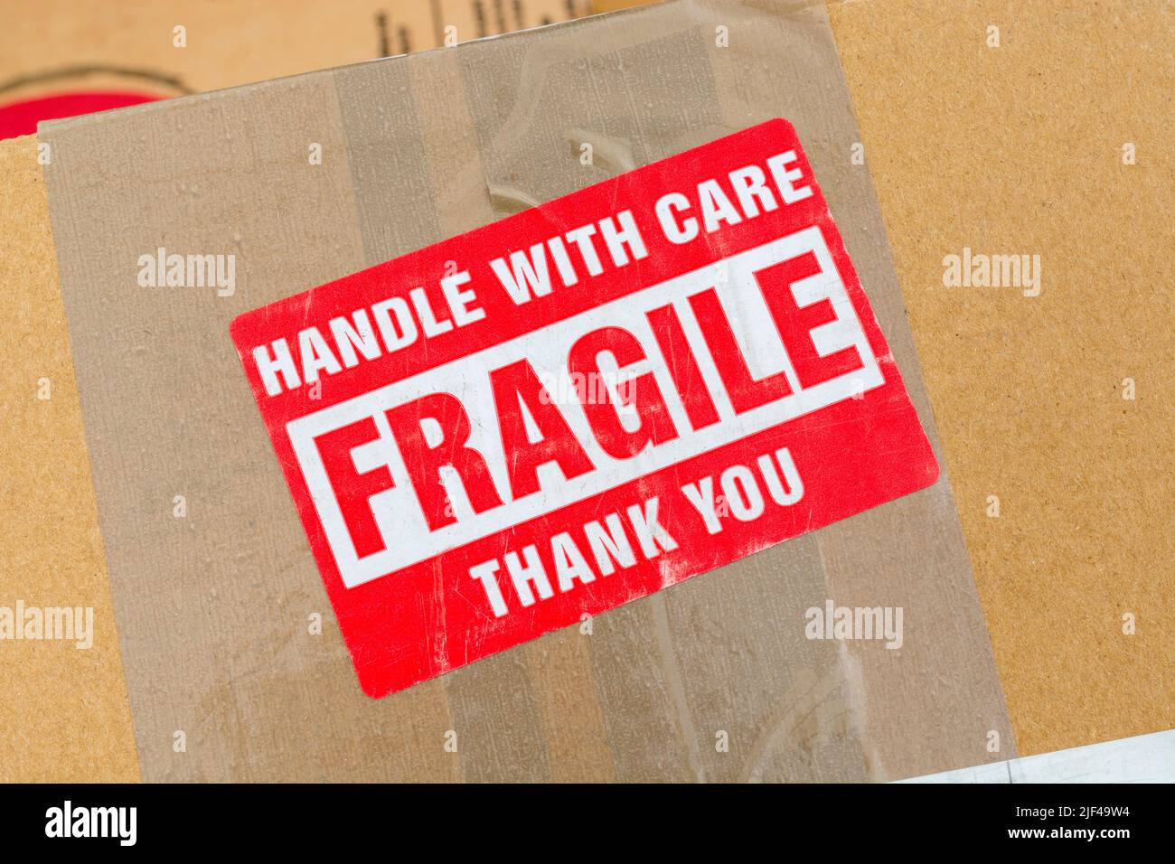 Versandkarton aus braunem Karton mit rot-weißem Aufkleber auf Haftpapier mit Aufdruck „Fragile“ und „Handle with Care“. Für etwas zerbrechliches und delikates. Stockfoto