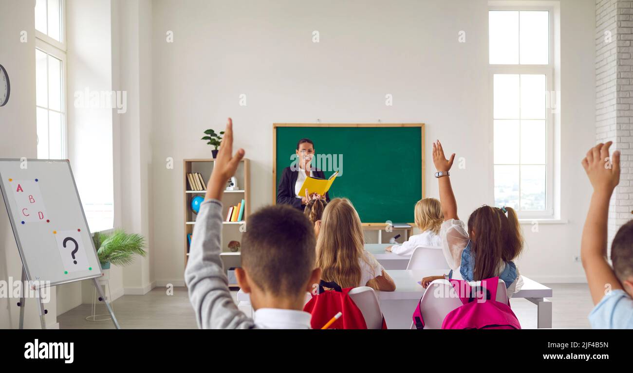 Gruppe von Grundschulkindern, die im Klassenzimmer sitzen und ihre Hände hochheben Stockfoto
