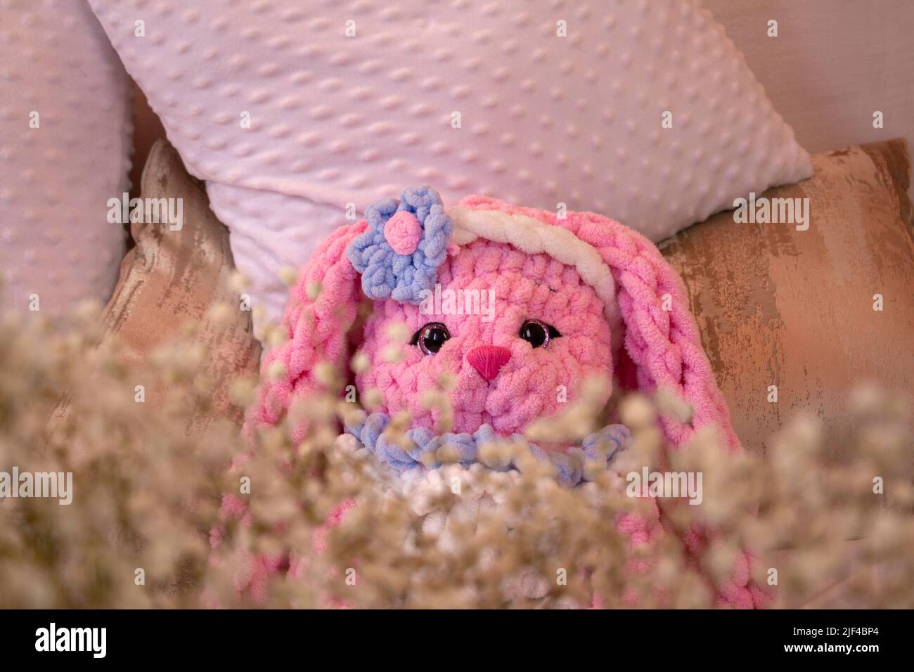 Auf dem Sofa sitzt ein pinkfarbenes Kaninchen-Strickspielzeug. Tierhäkel. Amigurumi. Für Text platzieren. Stockfoto