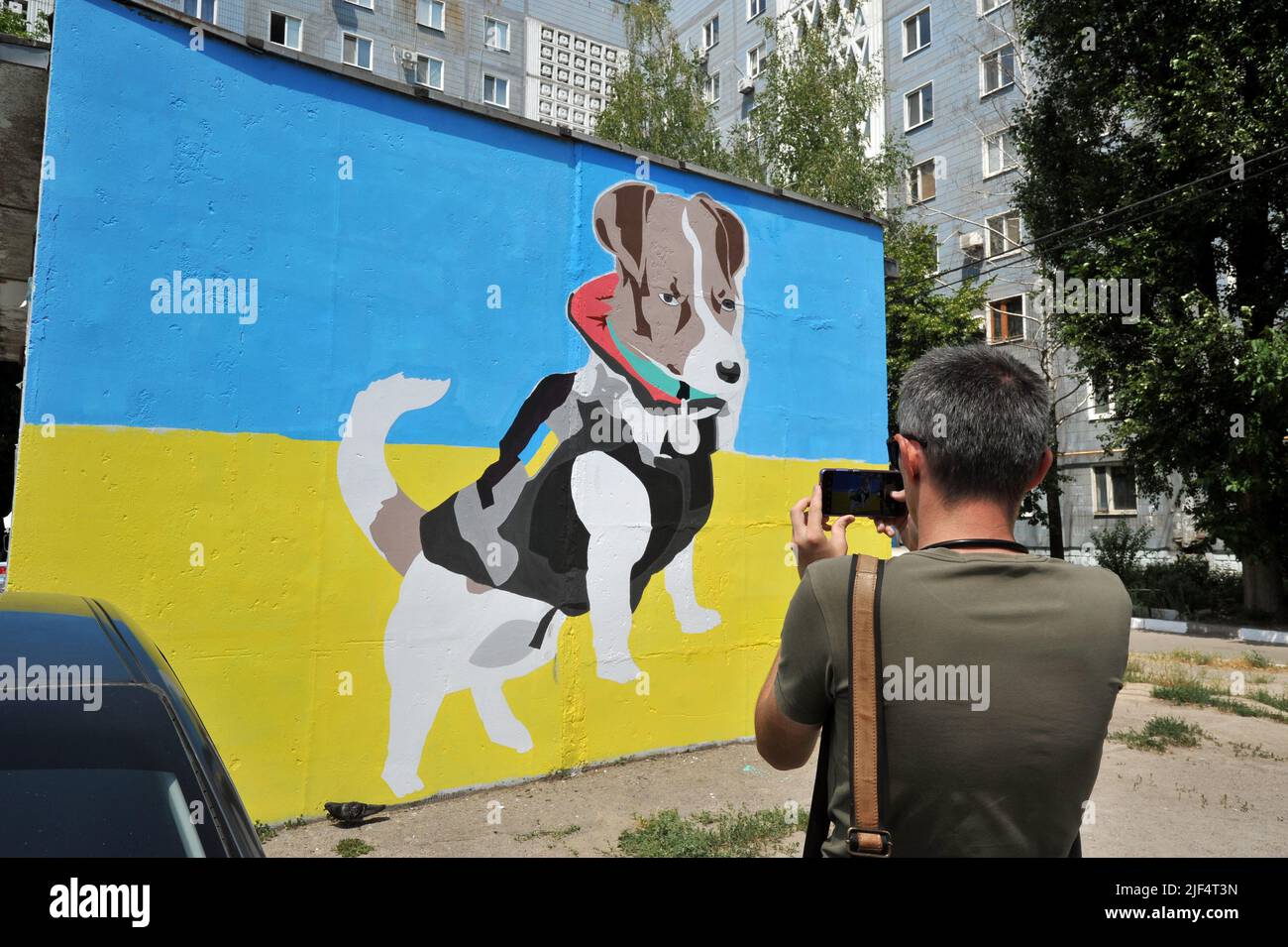 ZAPORIZHZHIA, UKRAINE - 29. JUNI 2022 - Ein Mann fotografiert ein Wandgemälde, das dem Schutzpatron des Sapper-Hundes gewidmet ist, an der Fassade eines örtlichen Hauses, Zaporizhzhia, im Südosten der Ukraine. Dieses Foto kann nicht in der russischen Föderation verteilt werden. Stockfoto