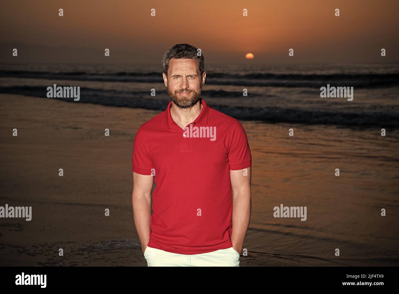 Sommerurlaub. Positive Emotionen. Lächelnder Mann mit Bart bei Sonnenuntergang über Meer. Stockfoto
