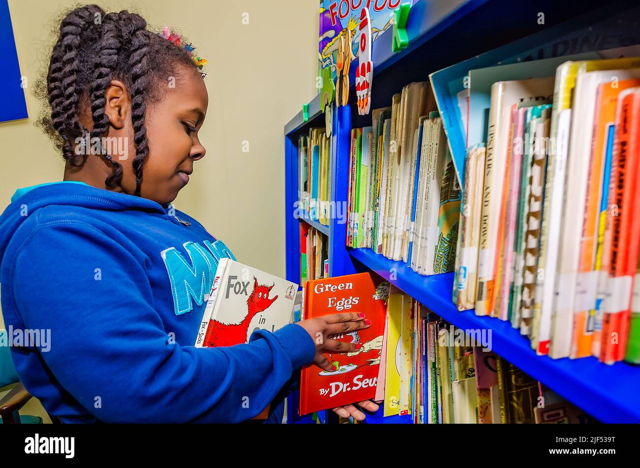 Ein afroamerikanisches Mädchen wählt Dr. Seuss-Bücher aus einem Bücherregal während eines Nachschulprogramms am 28. Februar 2013 in Columbus, Mississippi. Stockfoto