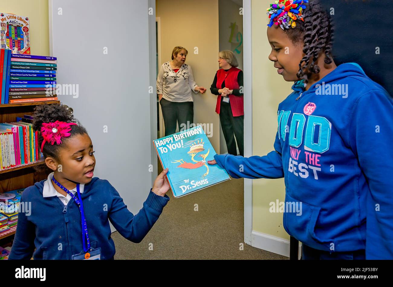 Ein afroamerikanisches Mädchen gibt einem jüngeren Kind während eines Nachschulprogramms am 28. Februar 2013 in Columbus, Mississippi, ein Dr. Seuss Buch. Stockfoto