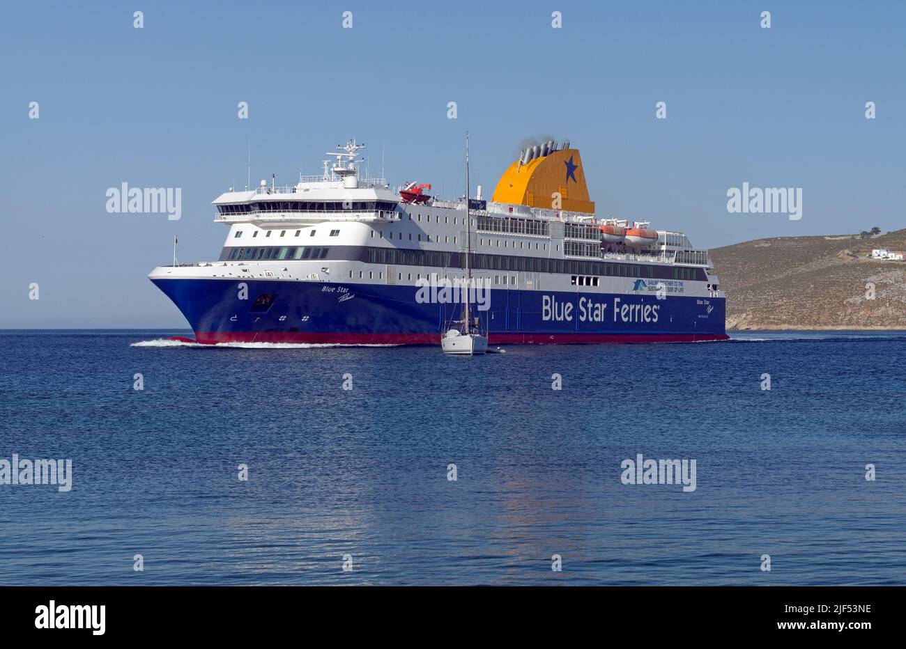 Blue Star, die Patmos Fähre, manövriert um ein kleines Segelboot, als sie zum Hafen von Livadia, Tilos Insel, in der Nähe von Rhodos anlegt. Mai 2022 Stockfoto