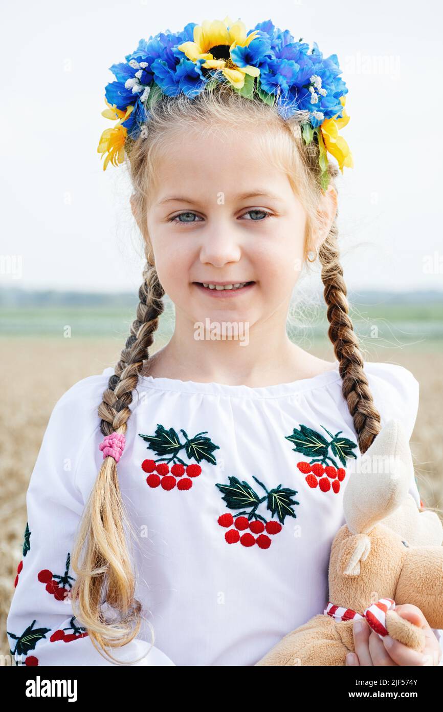 Porträt des Kindes in traditionellen bestickten ukrainischen Hemd und blau-gelben Kranz auf dem Kopf auf dem Hintergrund des Weizenfeldes an sonnigen Tag. Viburnum ist Symbol der Ukraine. Unabhängigkeitstag der Ukraine Stockfoto