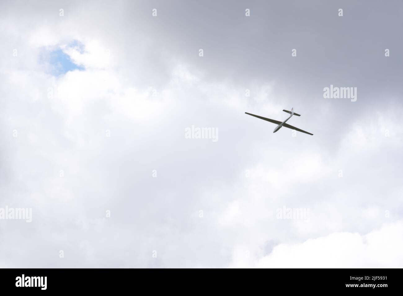 Segelflieger ohne Motor fliegt in dunklen Wolken über Hügeln Stockfoto