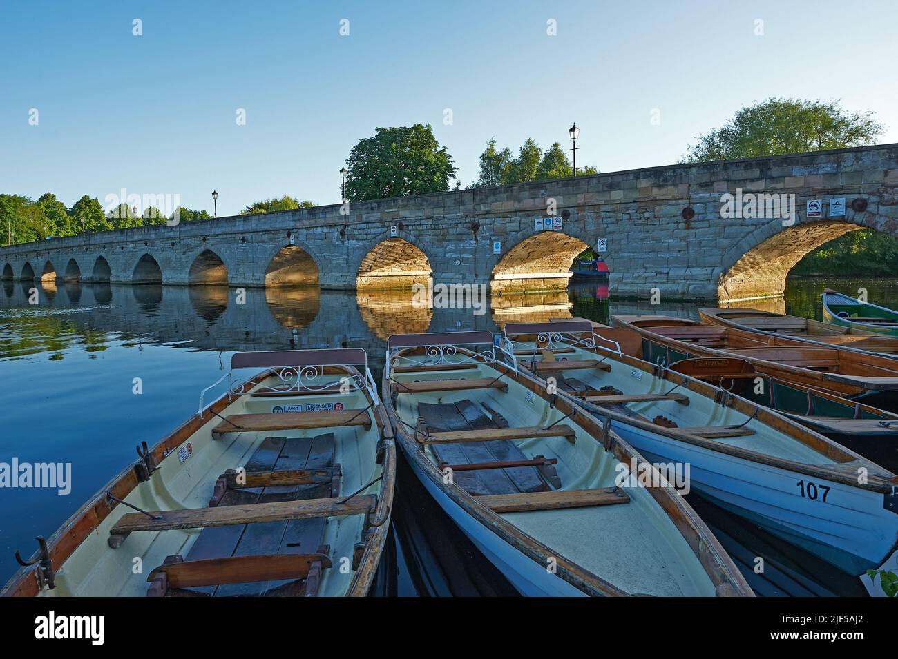 Tagesmiete Ruderboote, die auf dem Fluss Avon in Stratford-upon-Avon festgemacht sind, mit der Clopton Bridge im Hintergrund. Stockfoto
