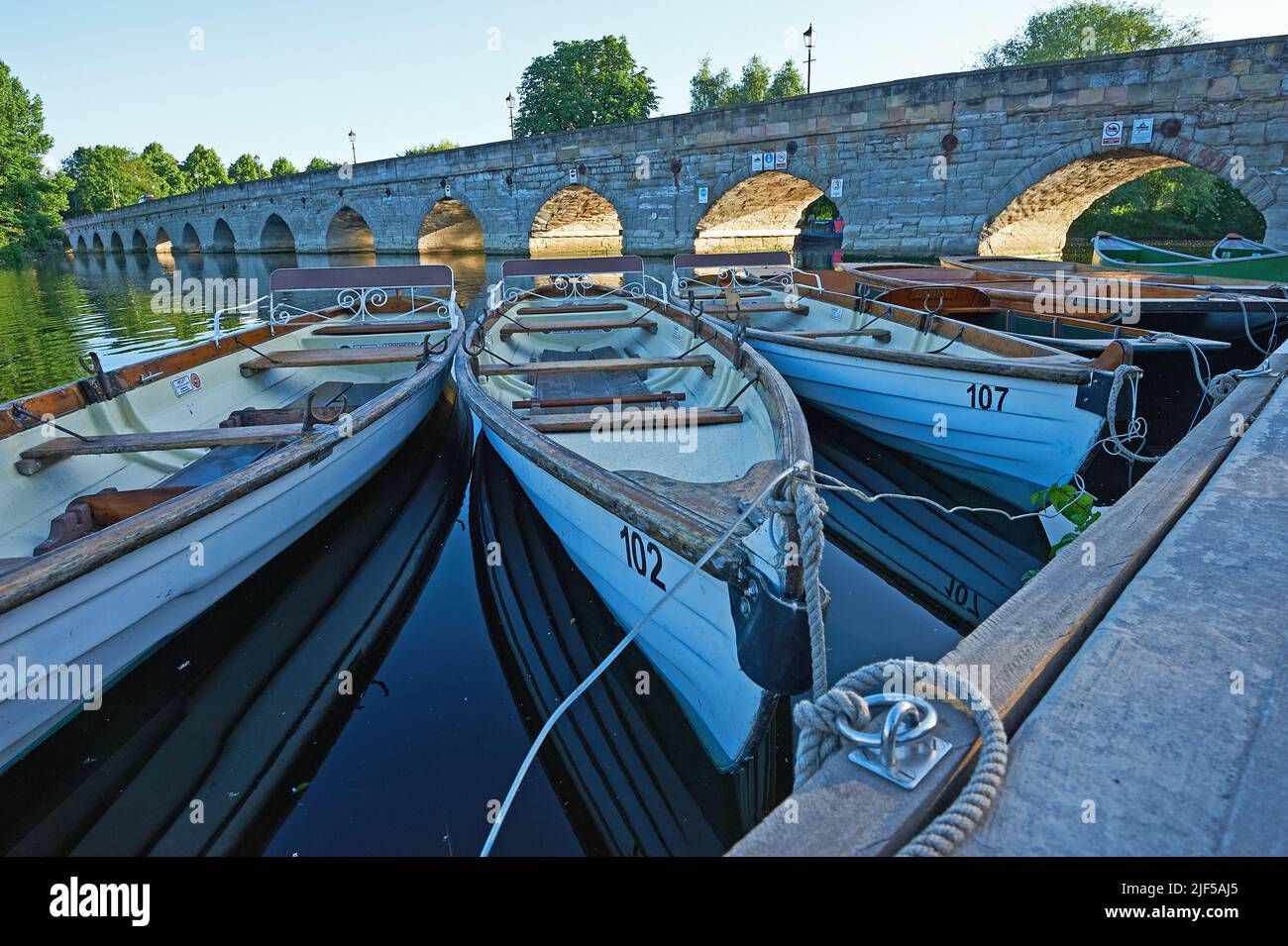 Tagesmiete Ruderboote, die auf dem Fluss Avon in Stratford-upon-Avon festgemacht sind, mit der Clopton Bridge im Hintergrund. Stockfoto