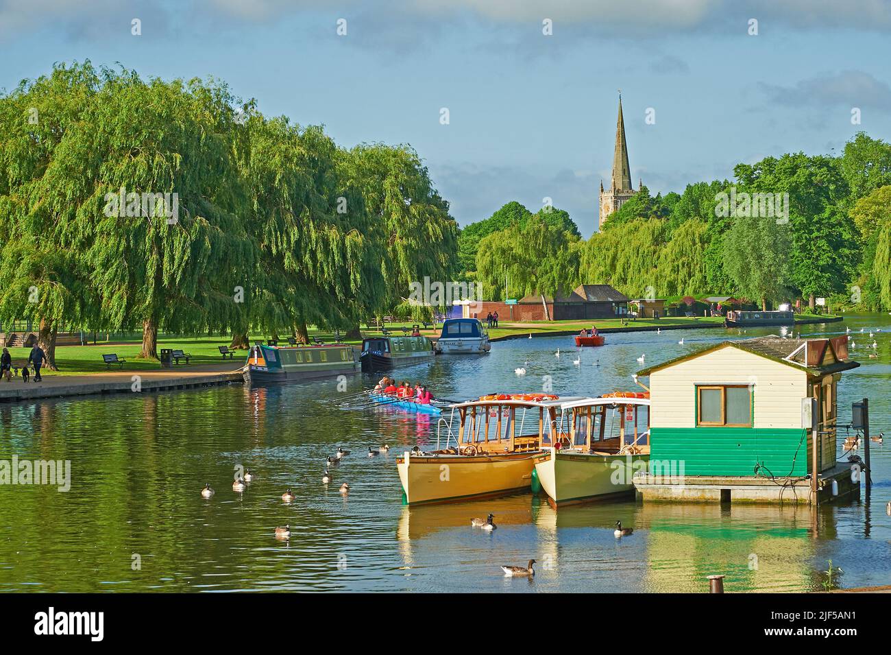 Blick entlang des Flusses Avon, Stratford-upon-Avon, Warwickshire in Richtung Holy Trinity Church, mit Touristenbooten, die vor Anker liegen. Stockfoto