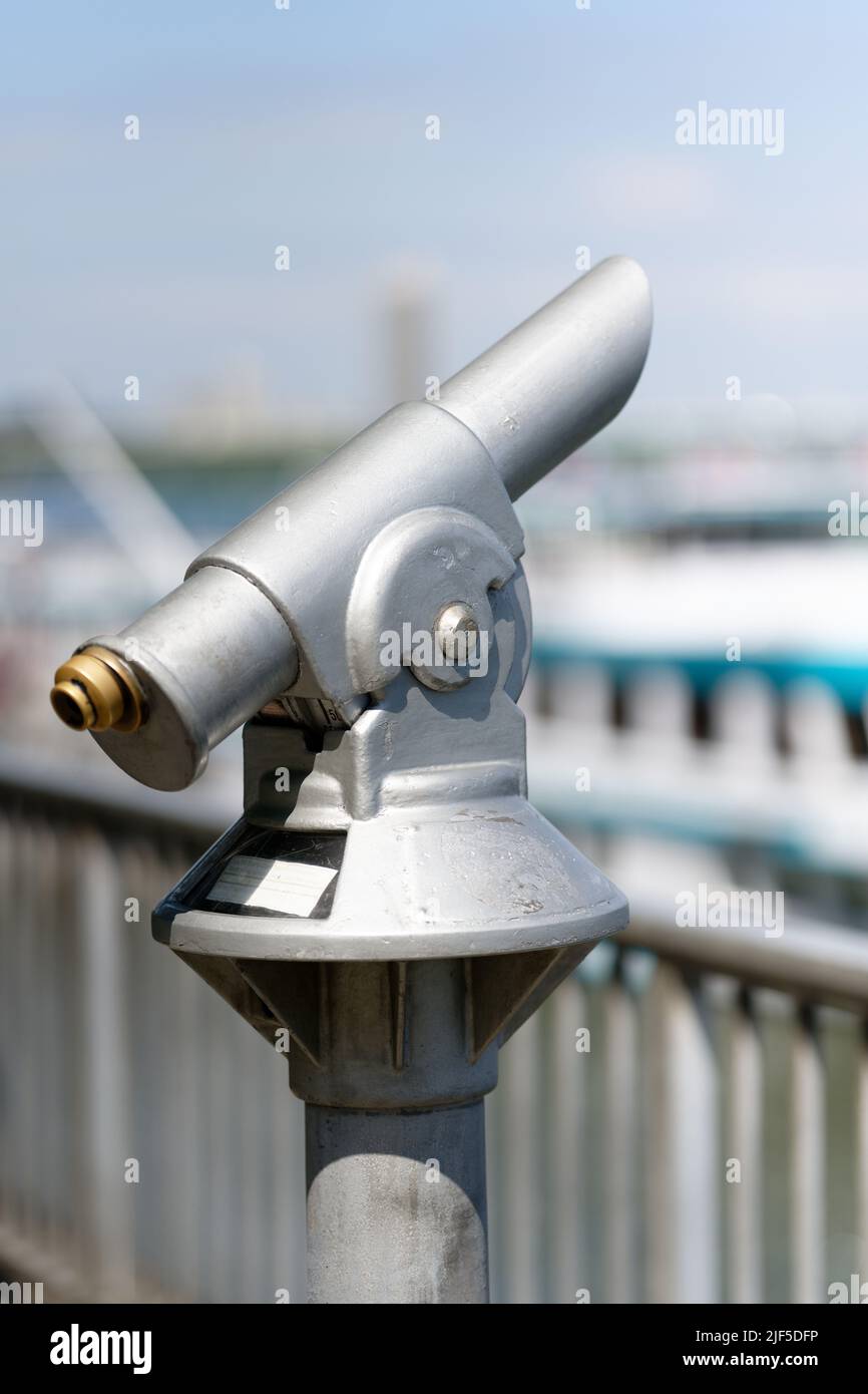 Münzfernrohr auf einem Flussufer mit Schiffen im verschwommenen Hintergrund Stockfoto