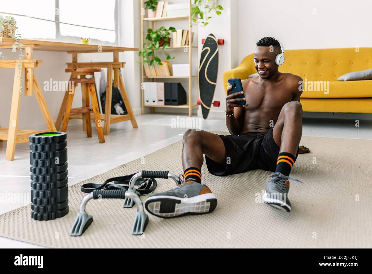 Ein sportlicher afrikanischer Mann, der nach dem Training zu Hause ein Mobiltelefon verwendet Stockfoto