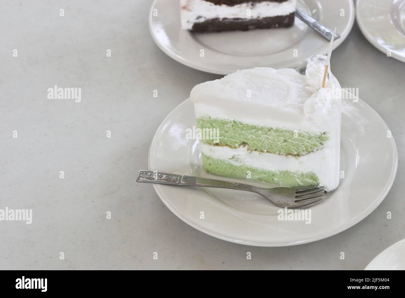 Japanischer Matcha grüner Tee mit Kokosmilchkuchen in Schale mit Löffel auf weißem Tisch Stockfoto