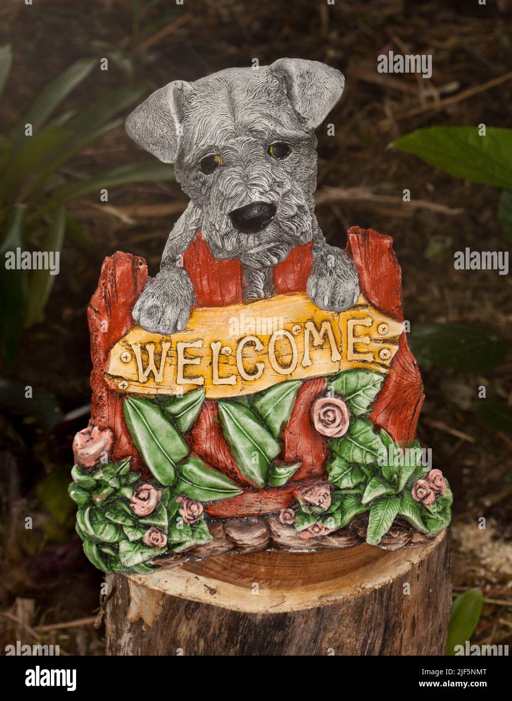 Ungewöhnliche und attraktive Betongarten Ornament - Highland Terrier Hund mit Pfoten auf Willkommensschild umgeben von Rosen und Blättern Stockfoto
