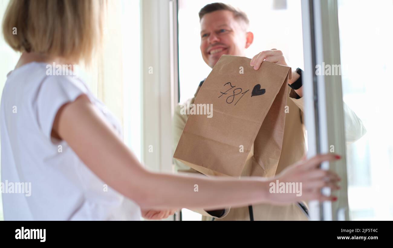 Frau erhält Paket vom Kurier mit Herz vor der Haustür Stockfoto