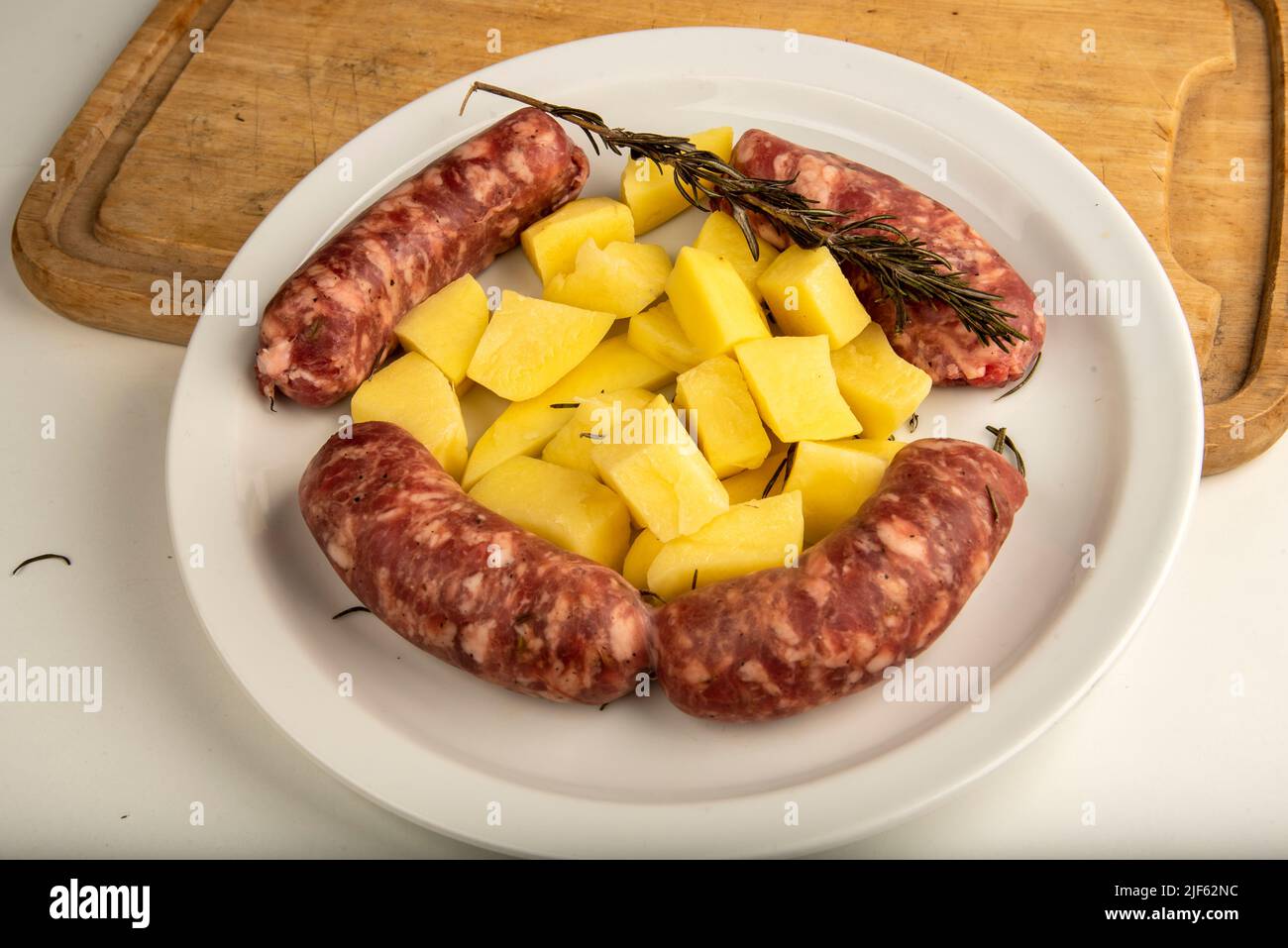 Verbinden Sie Würste mit frisch gebackenen Kartoffeln auf Holzschneidebrett isoliert auf weiß mit Kopierplatz. Stockfoto