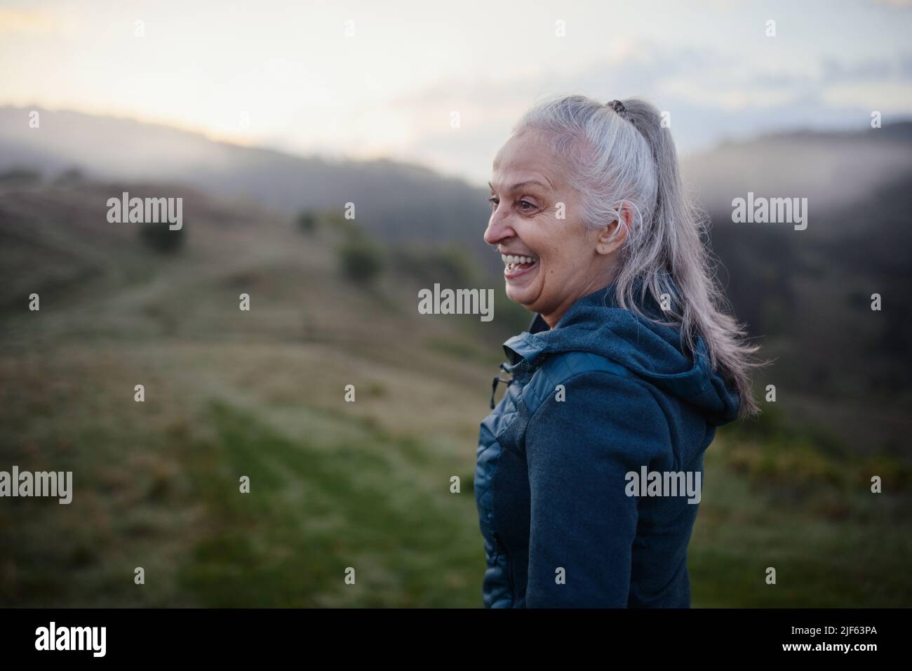 Ältere Frau, die am frühen Morgen in der Natur mit Nebel und Bergen im Hintergrund wandert. Stockfoto