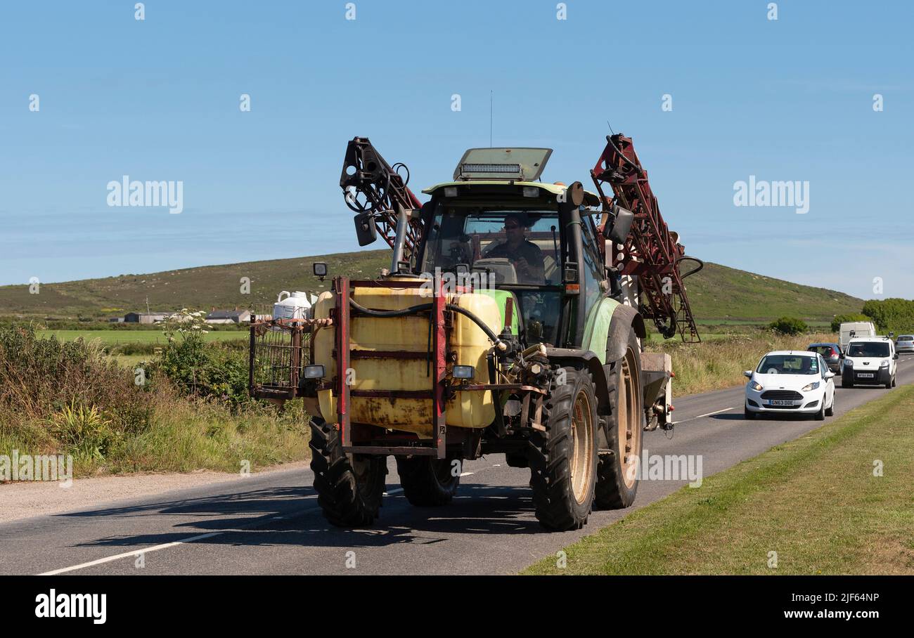 Cornwall, England, Großbritannien. 2022. Grüner Traktor mit montiertem Chemikalientank und Spritzgerät auf dem Heck, der entlang einer Landstraße in der Nähe von St fährt Stockfoto