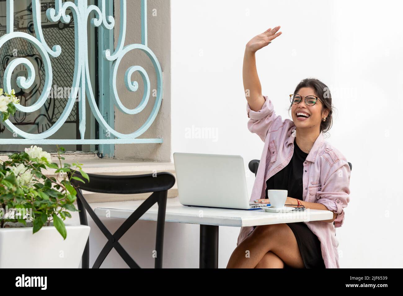 Junge Latina-Frau winkt, während sie im Bürgersteig-Café sitzt - Stockfoto Stockfoto