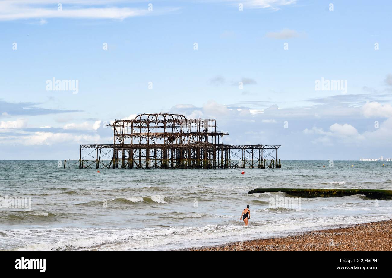 Brighton UK 30. June 2022 - ein Schwimmer am frühen Morgen genießt eine Mischung aus Sonnenschein und Wolken in der Nähe von Brighton's West Pier, da in den nächsten Tagen in Teilen von Großbritannien heisses, sonniges Wetter erwartet wird : Credit Simon Dack / Alamy Live News Stockfoto