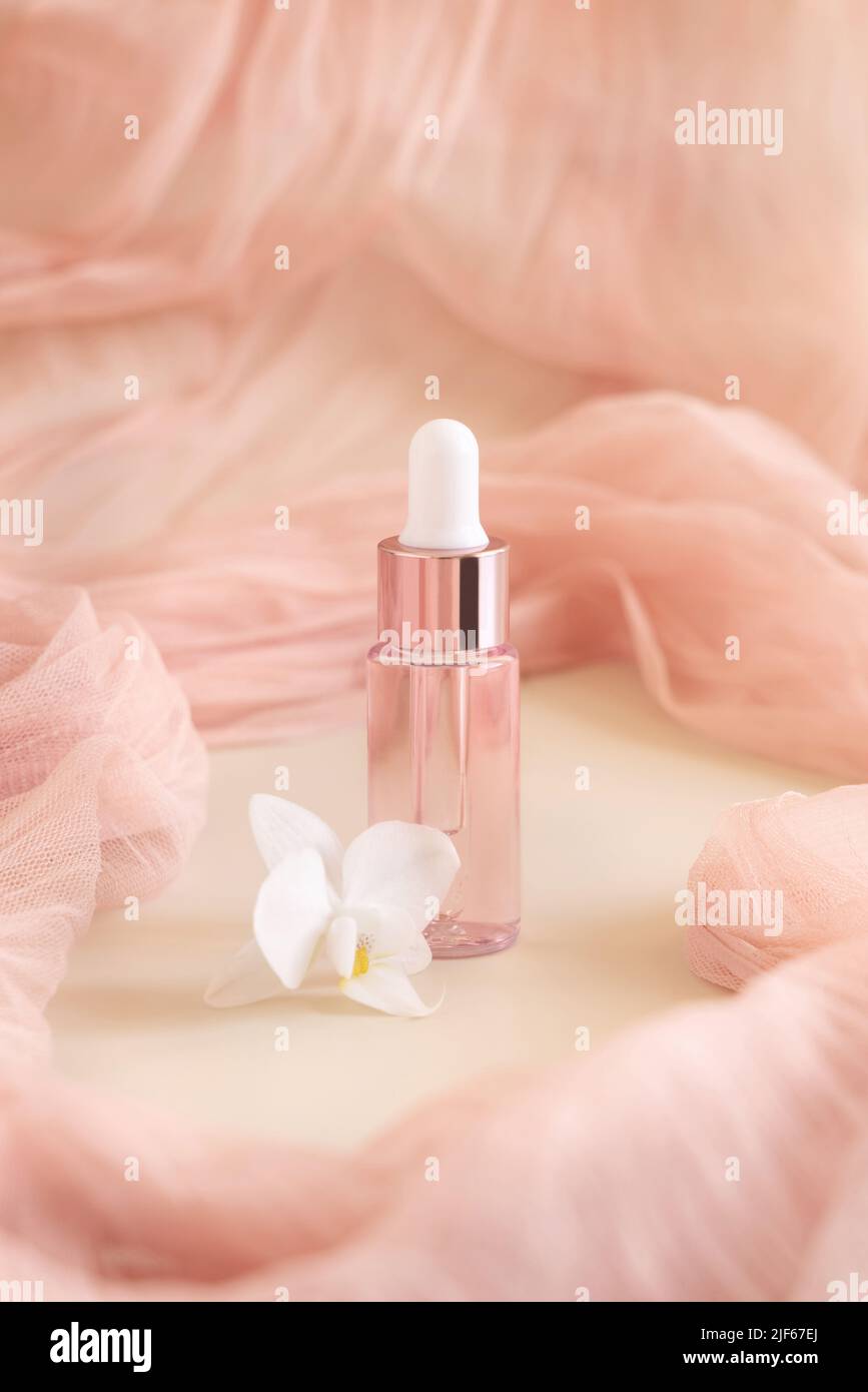 Hellrosa Tropfflasche in der Nähe der weißen Orchideenblüte auf hellgelb, Nahaufnahme, Mockup. Hautpflegeprodukt, aromatisches Öl oder Serum. Exotische Kosmetik Stockfoto