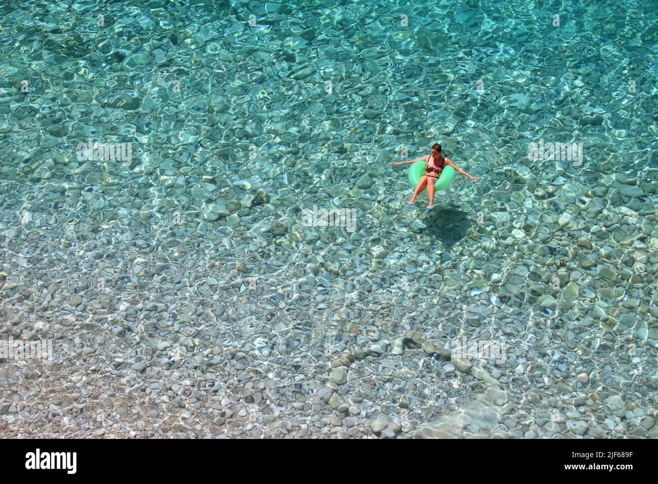 Touristenfrau schwimmend auf aufblasbarem Spielzeugrad in klarem Wasser. Kroatien Sommer. Pasjaca Strand unter den Klippen in Konavle. Stockfoto