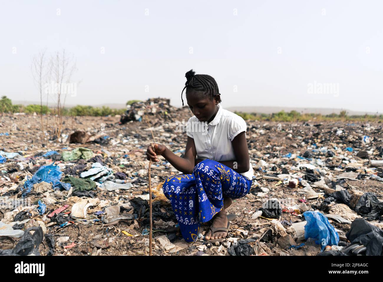 Afrikanisches Mädchen, das inmitten von Abfallhaufen sitzt und für die Suche nach recycelbaren Materialien wie Metall, Glas und Kunststoff verantwortlich ist; informelle Abfallrezyk Stockfoto