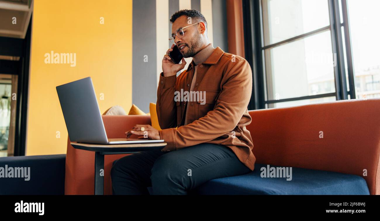 Geschäftsmann, der am Telefon spricht und einen Laptop in einem Co-Working-Raum benutzt. Zielgerichteter junger Unternehmer, der mit seinen Geschäftspartnern Pläne macht Stockfoto